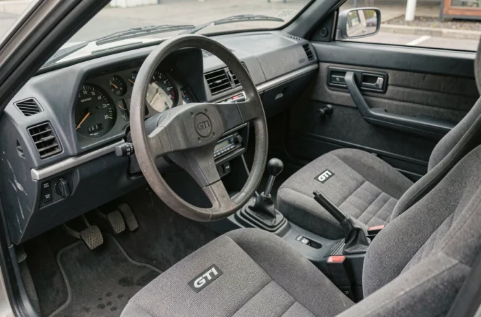 Intérieur authentique d'une Peugeot 305 GTI avec tableau de bord d'époque, sièges baquet en tissu et volant sport des années 1980